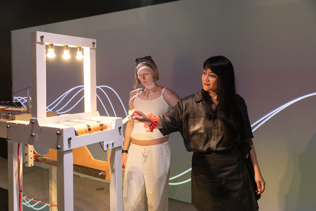 Two people turn a handle on an installation with dramatic line projections behind