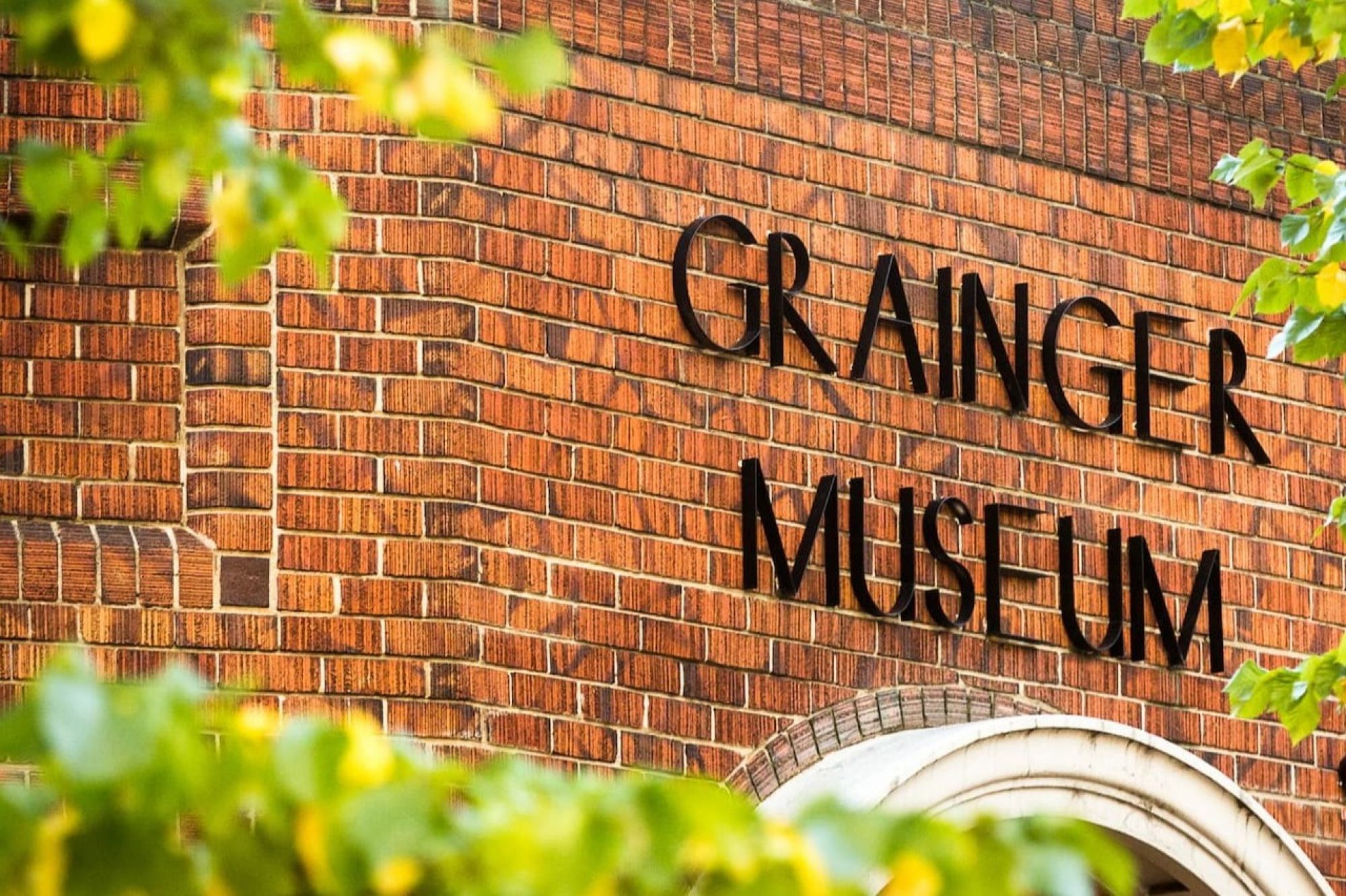 An exterior shot of the front of The Grainger museum with trees in foreground